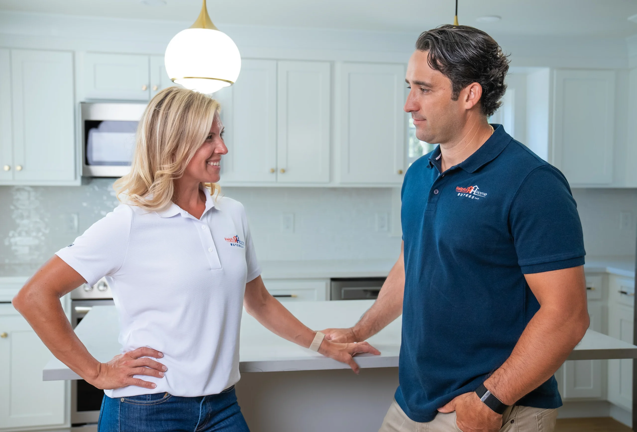 Meghan and Dan standing in a kitchen that was renovated by Helpful Home Buyers, wearing polo shirts with the HHB Logo.